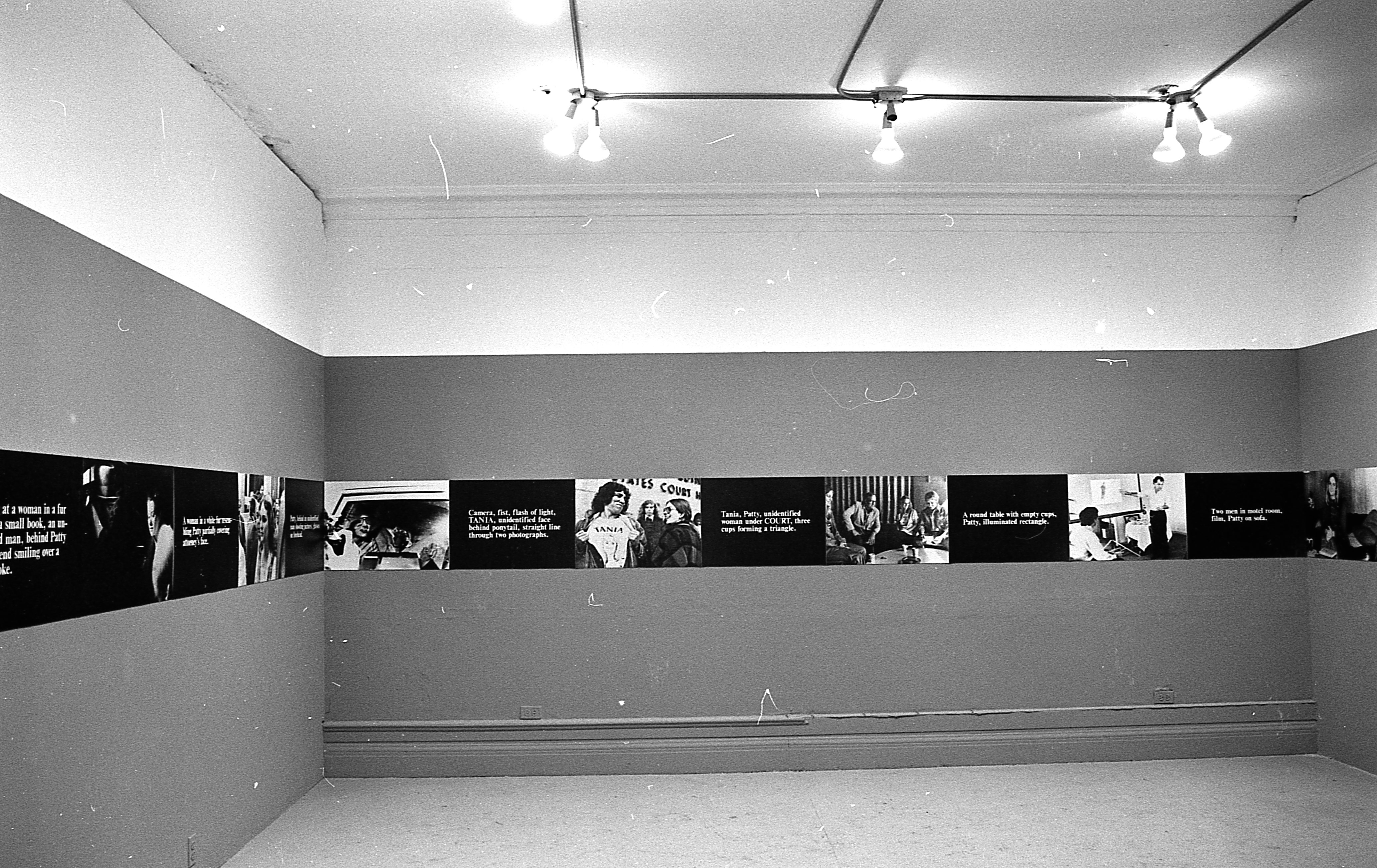 A continuous strip extends around the perimeter of the room, hung up on the walls. The strip alternates between photographic stills and black boxes overlaid with white text.