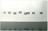 A photograph of a white gallery wall with multiple photographs mounted in a crooked row.