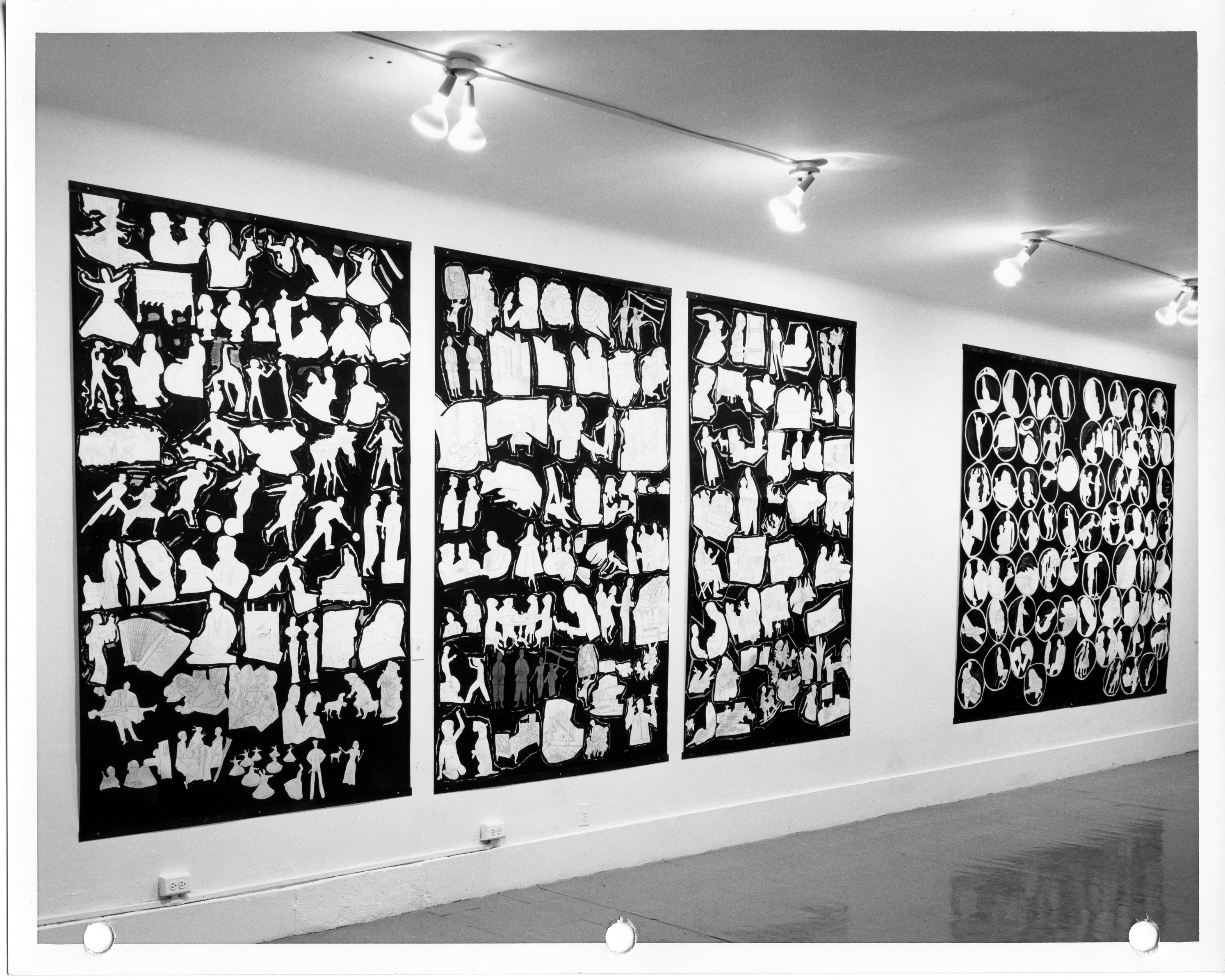 A black and white installation photograph. Four black rectangular panels hang on the wall. Each one is filled with white silhouetted shapes of human figures, and objects.