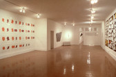 A large room with white walls. Artworks hang on the right and left walls, covering most of the surface area. There is a door open towards the back of the room.