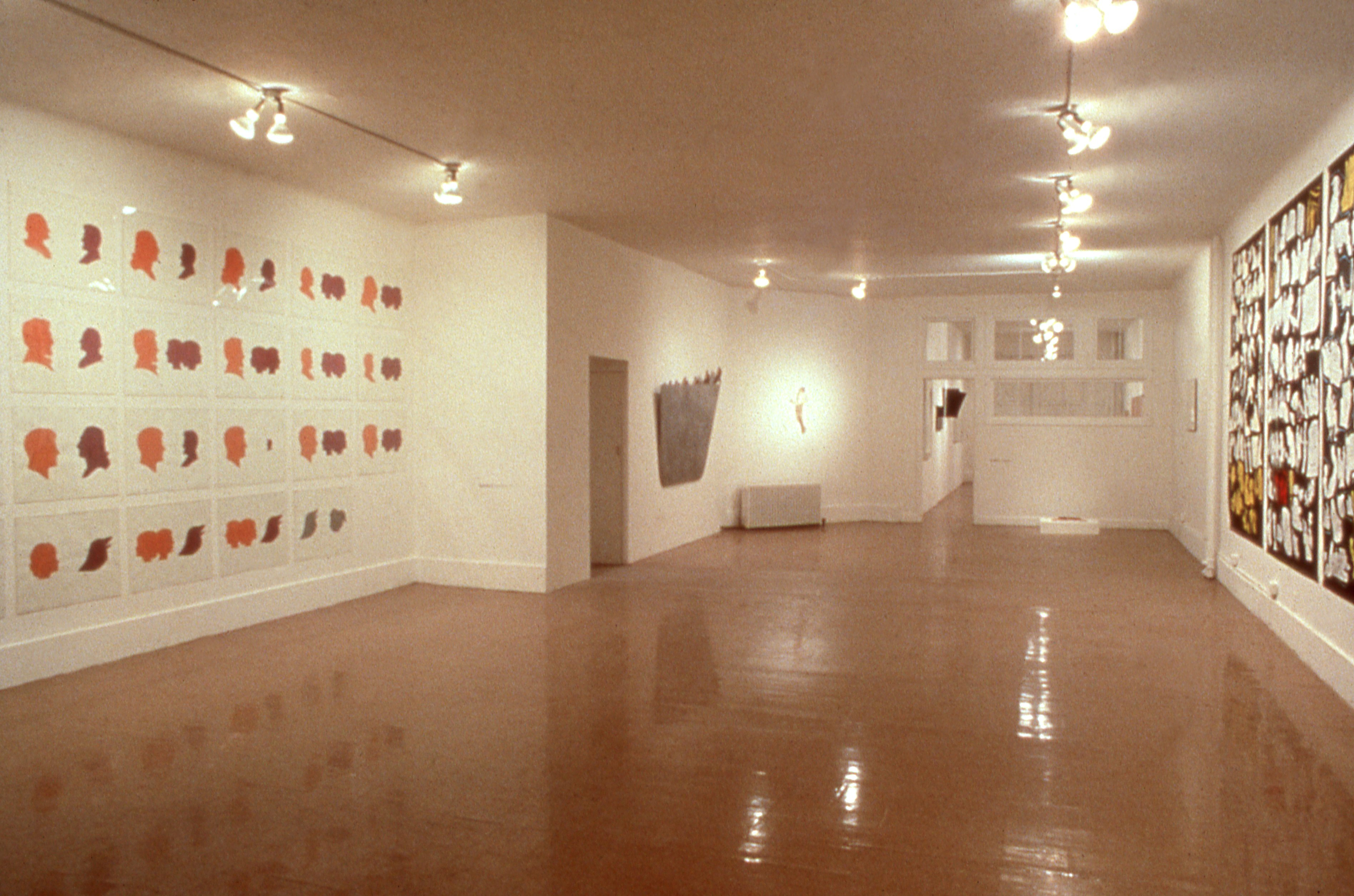 A large room with white walls. Artworks hang on the right and left walls, covering most of the surface area. There is a door open towards the back of the room.