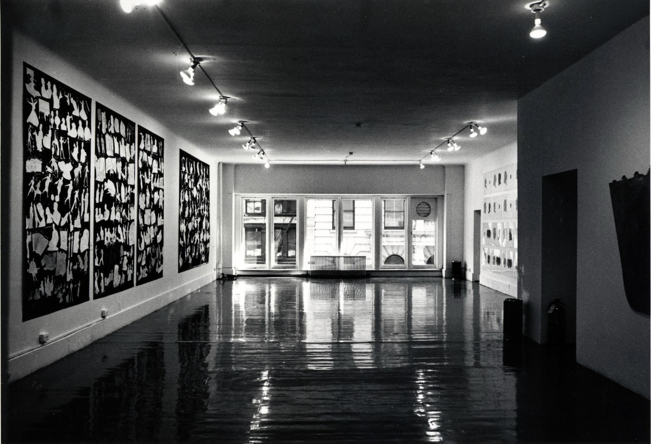 [Artworks hang on walls on the left and right. In the background, a neighboring building is visible through the window.]