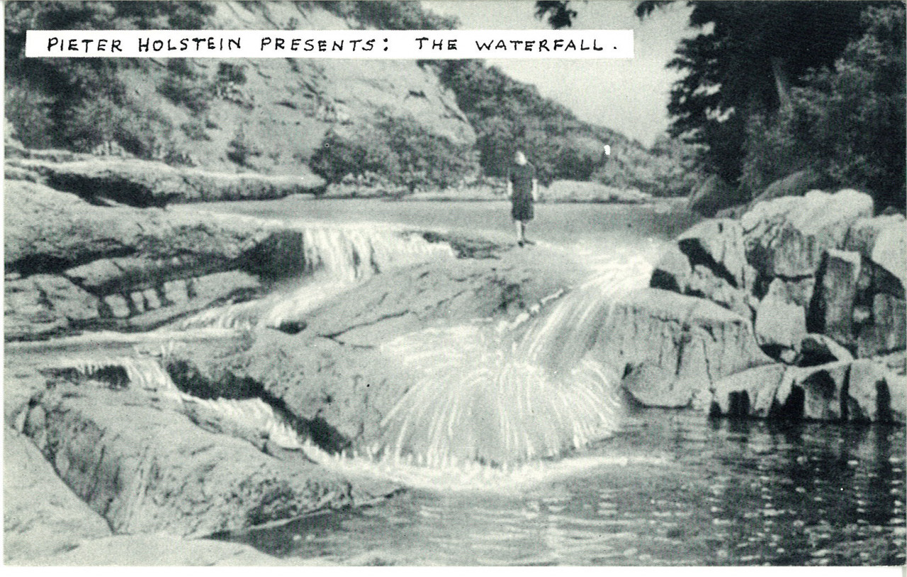 A man stands on top of a rock formation. Water from a nearby stream falls over the rock formation into a shallow pool. Text at the top of the image reads, 