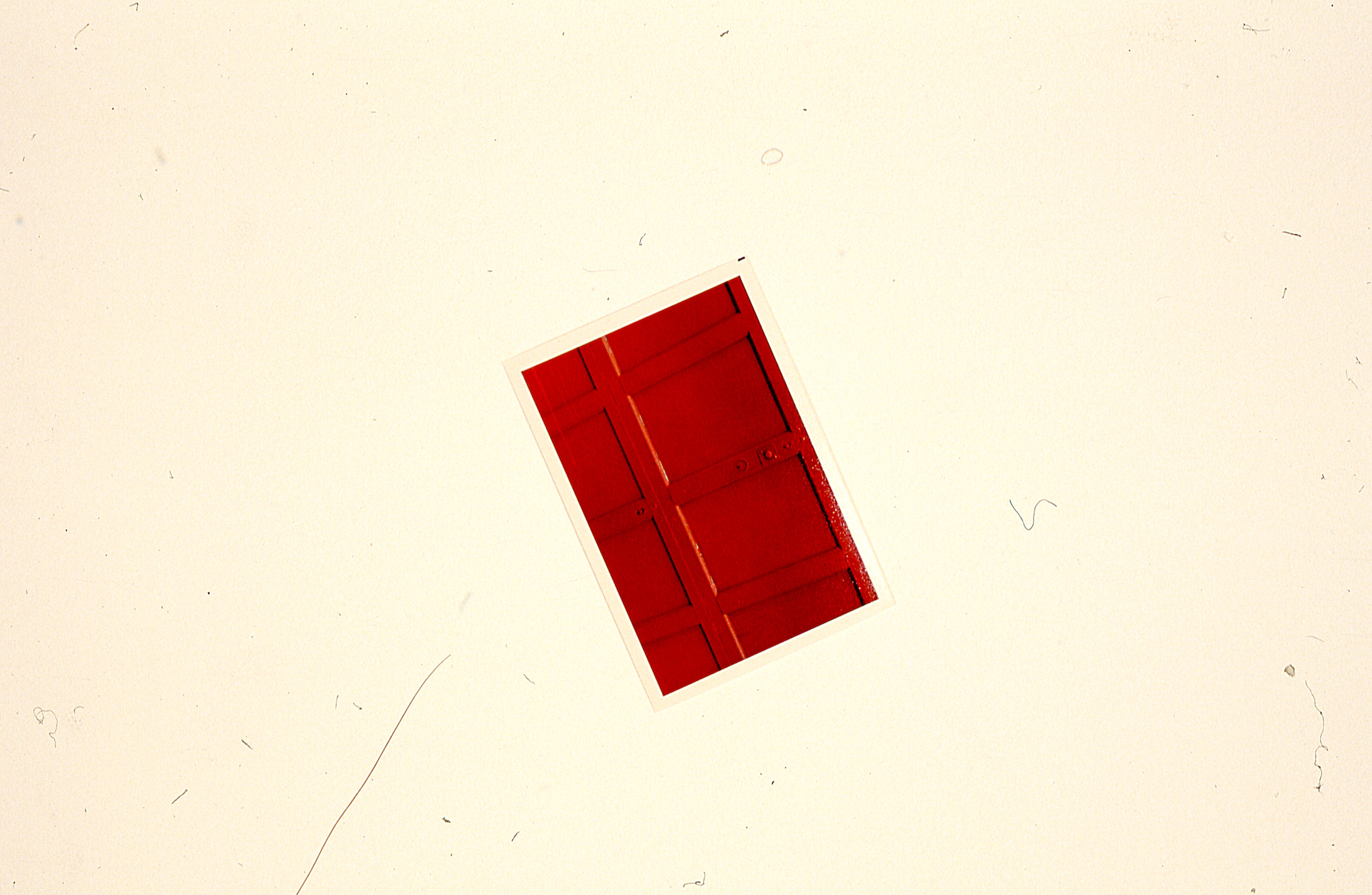 One red photograph is mounted at an angle on a white gallery wall.