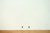 Two small photographs are mounted on a white gallery wall.