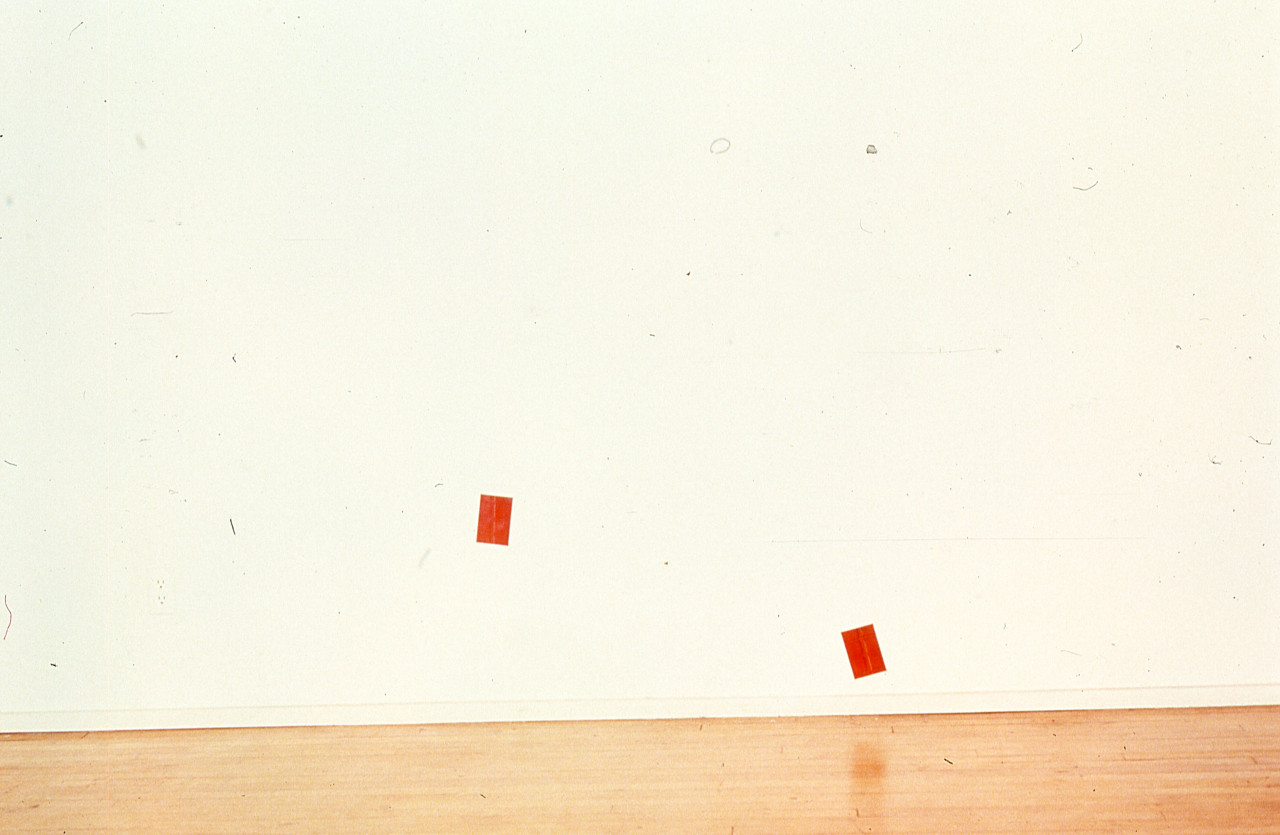 Two red photographs are mounted on a white gallery wall.