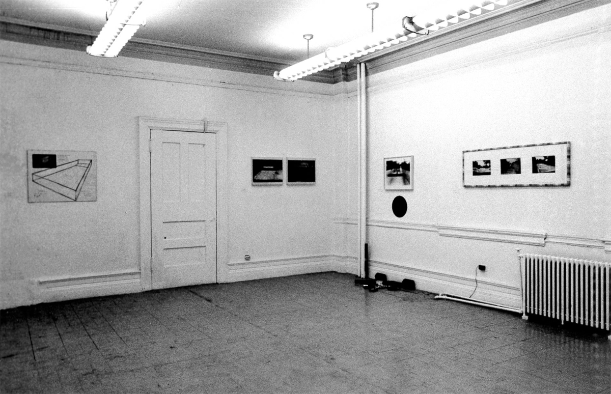 Frame photographs and text hang on the wall in a gallery space.