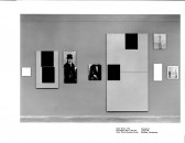 A line of eight paintings and blocks of illegible text in various sizes hang on a wall.  Some are paintings abstract compositions of black squares, others show a person in period dress, and two show the Eiffel Tower.