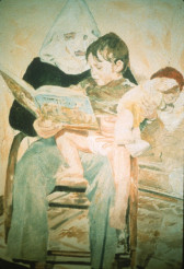 An adult sits in a chair and reads a book to a child seated on their lap and holding a doll.  The adult wears wears a white, pointed, Klu Klux Klan-style hood.