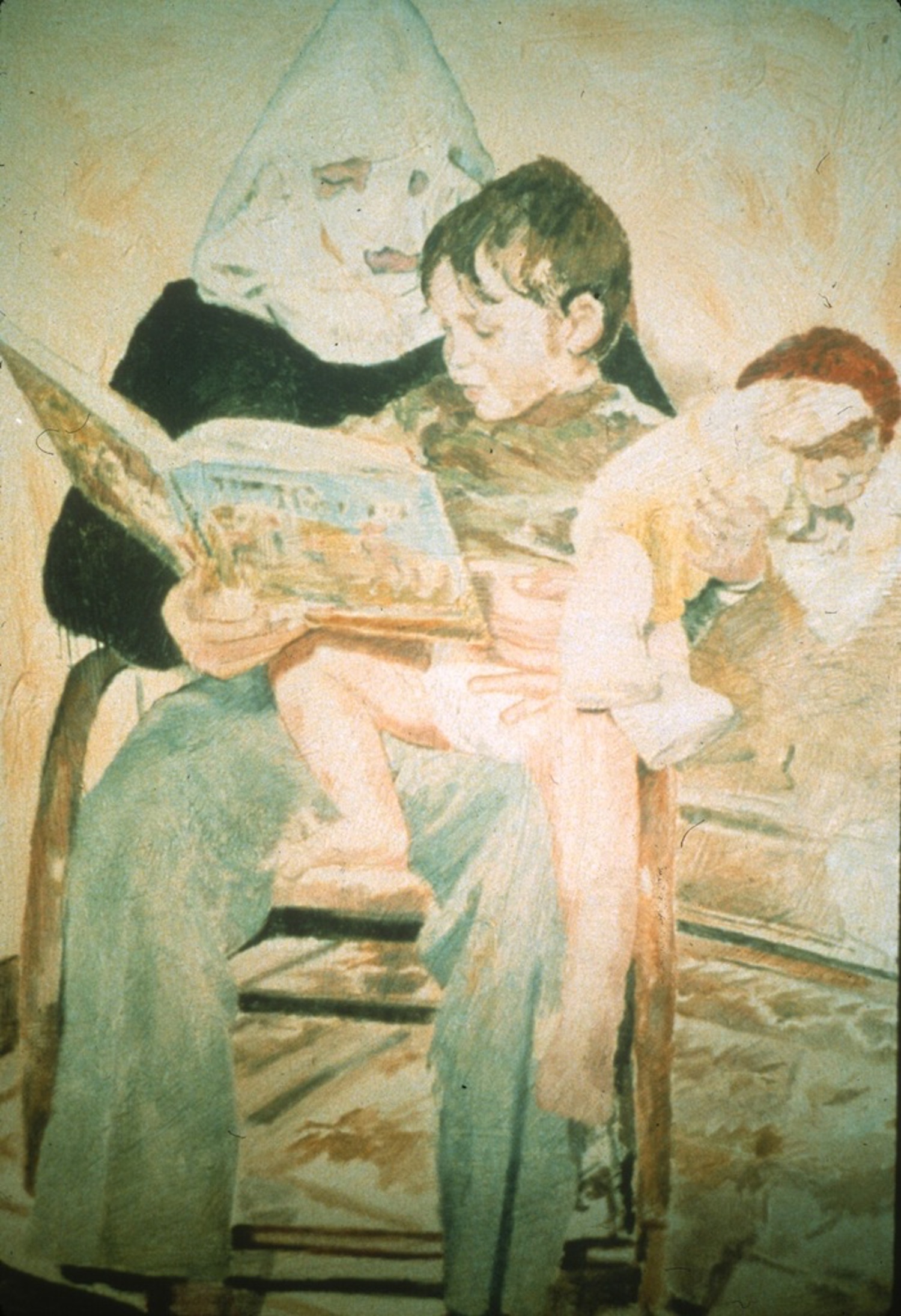 An adult sits in a chair and reads a book to a child seated on their lap and holding a doll.  The adult wears wears a white, pointed, Klu Klux Klan-style hood.
