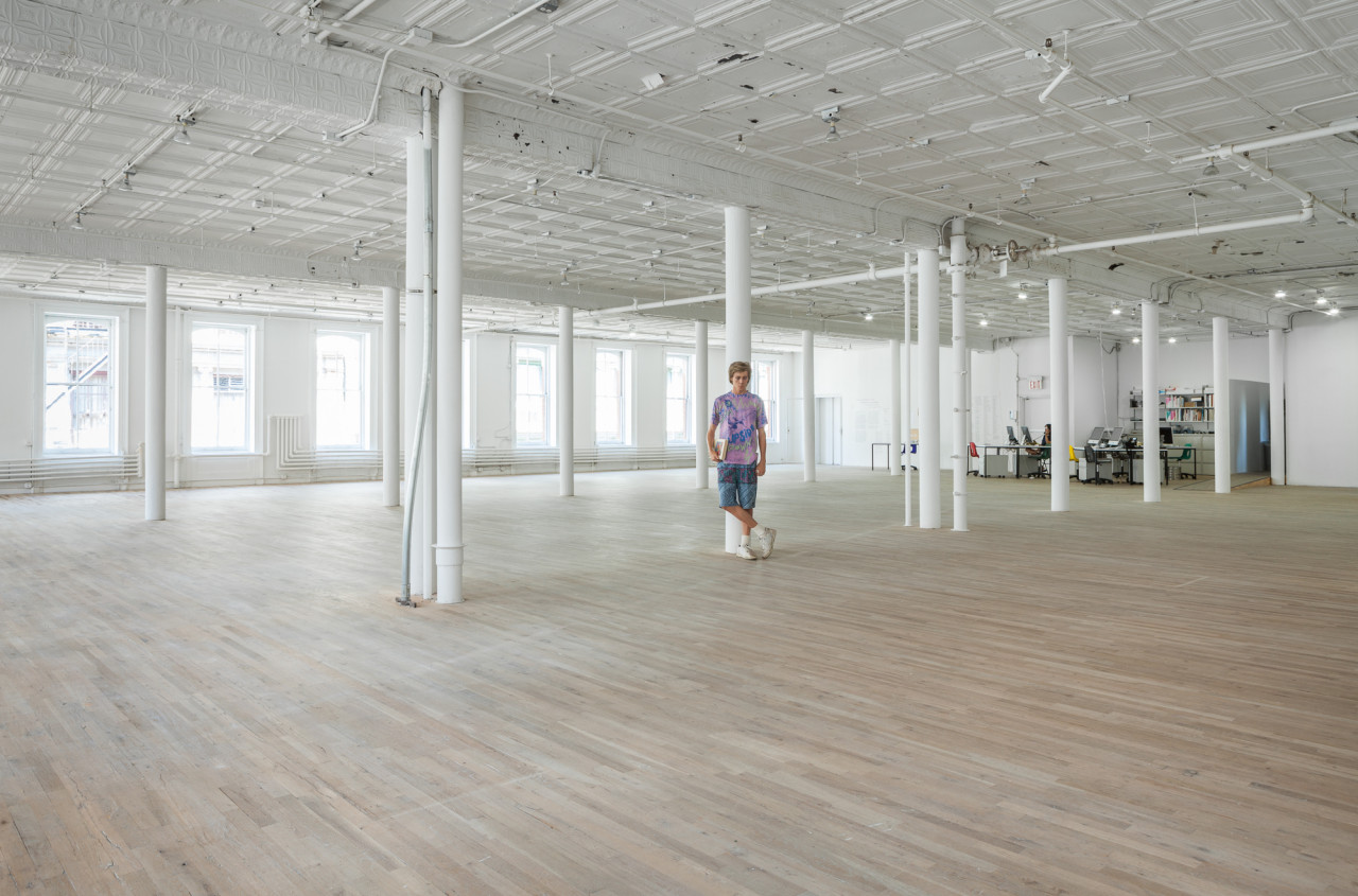 A sculpture of a man leans against a white column in an otherwise empty gallery space.