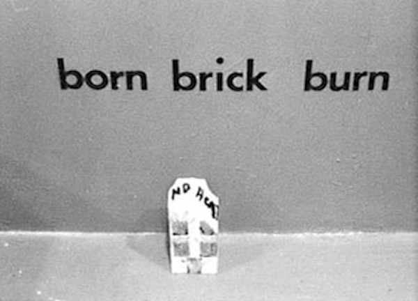 A brick on the bround with black text on it that reads, "No heat." Above this brick in black lettering on the wall is text that reads from left to right, "born brick burn."