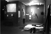 A view of a bedroom with various poster images on the walls and a dotted line cloth on a matress lying on the floor.