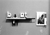 Sculptural white lettering appears on a shelf starting with 'b', but then a figure's torso appears and then the letters 