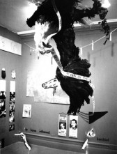 A large taxidermied eagle hangs upside down from the ceiling holding line tape that repeats 