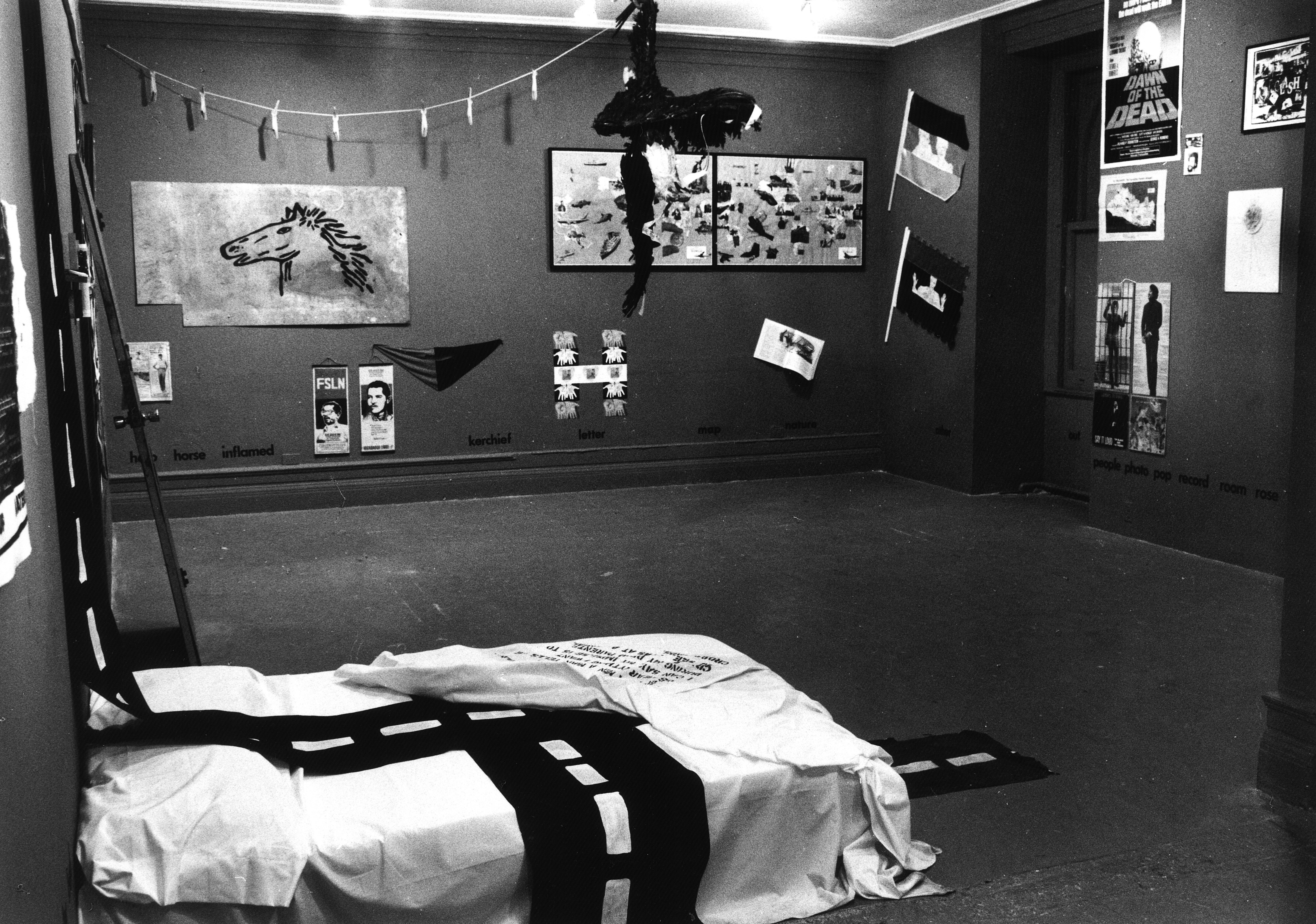 A view of a bedroom with various imagery on the walls along with a line and clothespins and a dotted line cloth on a matress lying on the floor.
