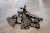 Color image of a pile of freeway rubble arranged on the floor, with a sculpture of a bird made of a deconstructed Nike sneaker perched on top of the pile, with its wings spread.