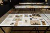 Three large display cases exhibit various objects. The case most within sight displays drawings, posters, photogrpahs, newspaper clippings, and a small sculpture.