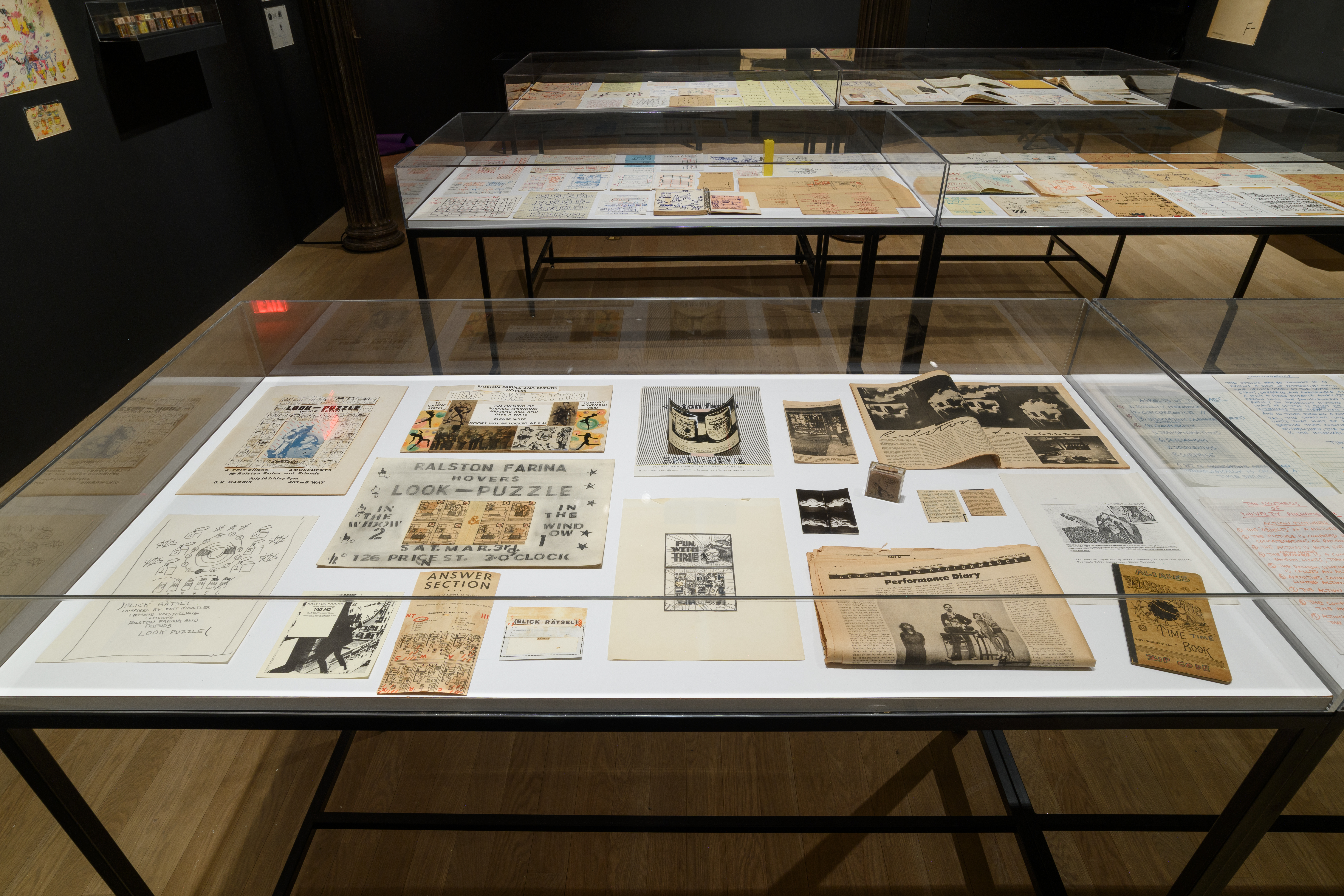 Three large display cases exhibit various objects. The case most within sight displays drawings, posters, photogrpahs, newspaper clippings, and a small sculpture.