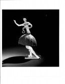 A small constructed dancing figurine appears on a pedestal with light shining on it from the right creating a shadow on its left.
