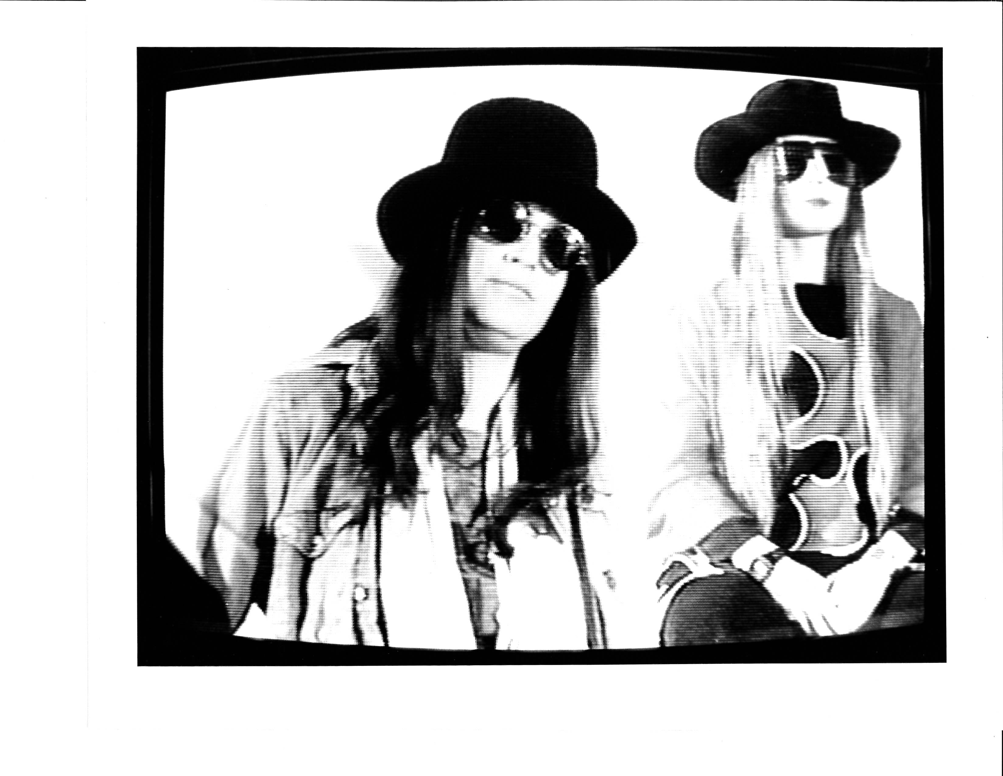 Two people with hats, sunglasses, and long straight hair. One looks into the camera, the other diagonally past.