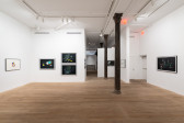 A color image of a gallery space with two columns in the middle. Framed drawings depicting colorful abstract compositions hang on the white walls. Five of the drawings are made on black paper, and two on white paper.