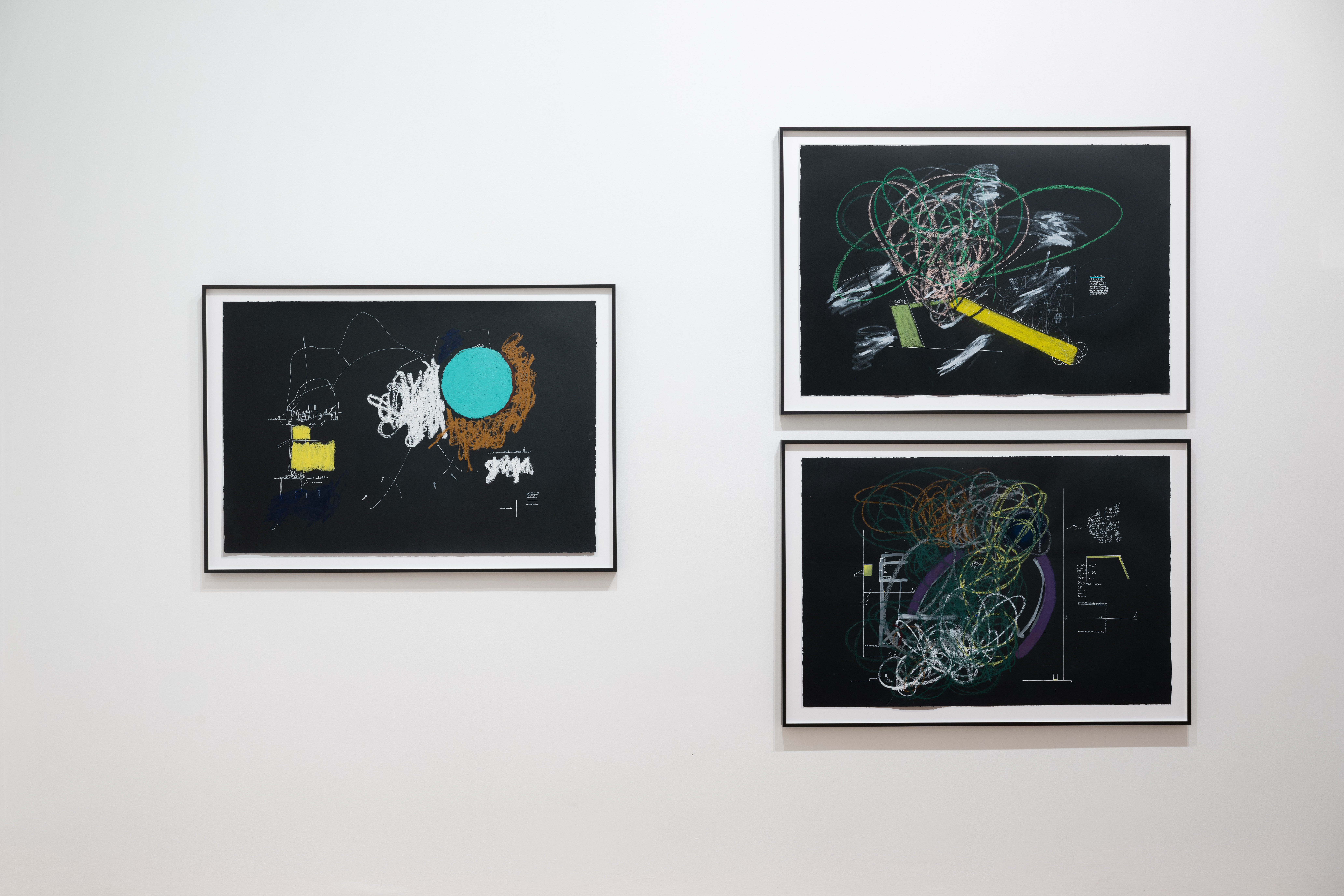 A color image of three framed works against a white wall. The drawings are done on black paper and depict abstract compositions made up of white, and colorful shapes, lines and strokes.