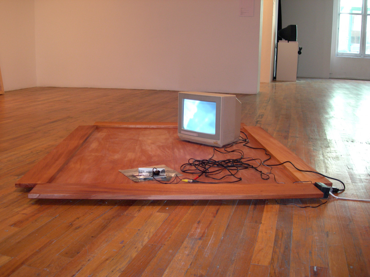 A gray television sits on a rectangular wooden board. There is a mass of wires next to it that snakes towards a pile of nearby photographs.