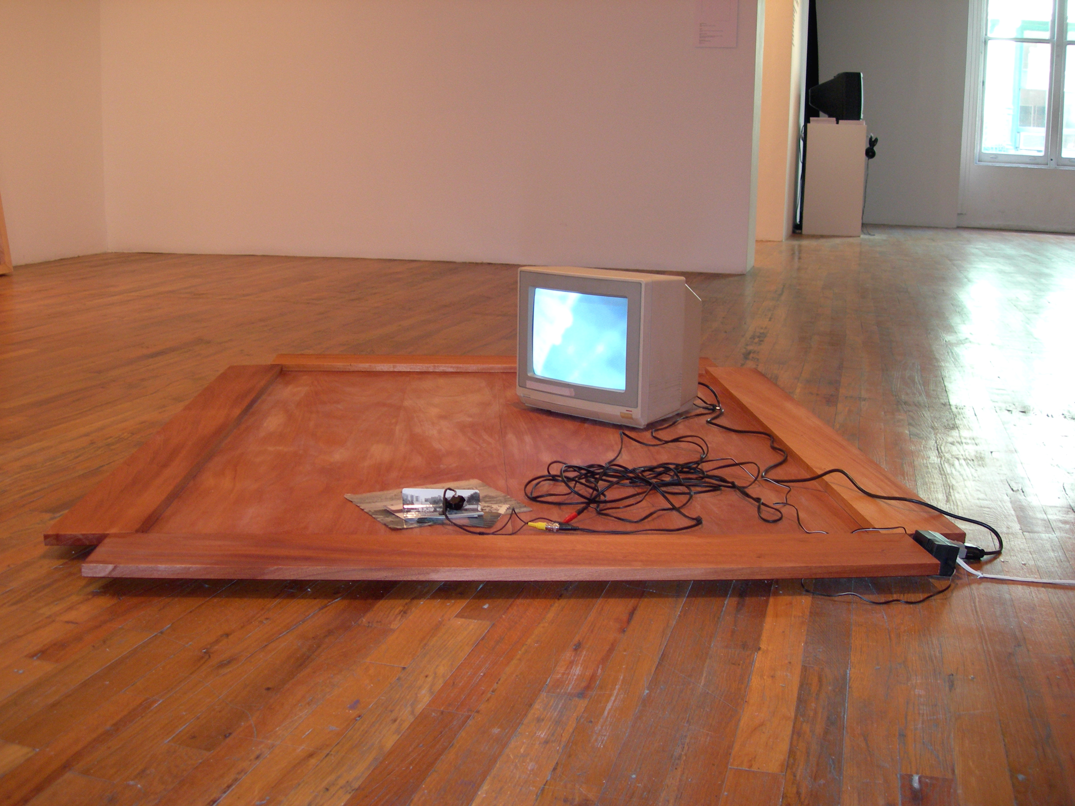 A gray television sits on a rectangular wooden board. There is a mass of wires next to it that snakes towards a pile of nearby photographs.