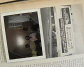 A sideways image of a photograph sitting on top of an open book. The photographs shows four people sitting next to each other. The book page is split with a column of text and a black and white image of a billboard that reads, 