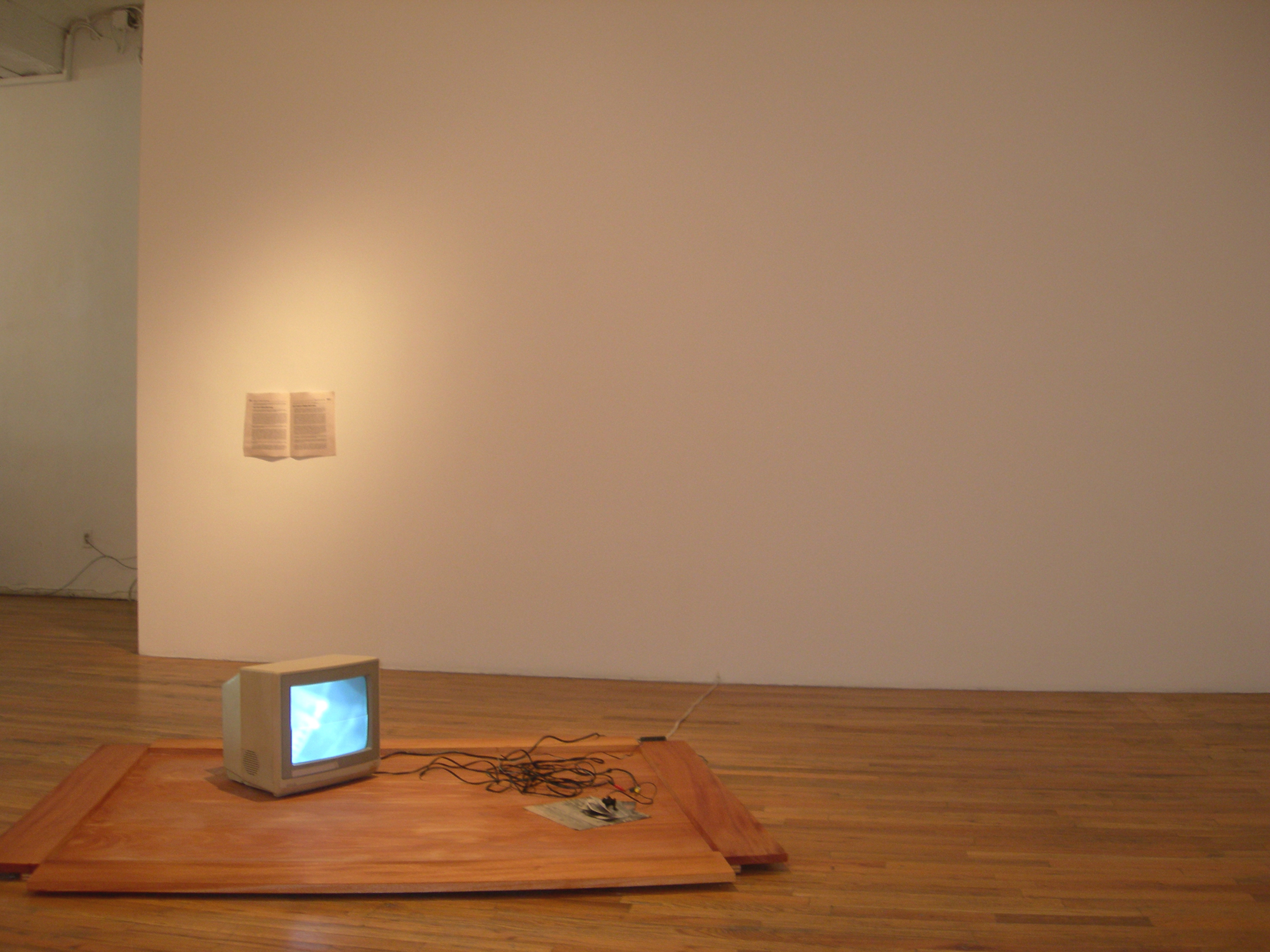 A gray television sits on a rectangular wooden board. There is a mass of wires next to it. In the background, a white paper with black text hangs on a white wall.
