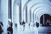 A negative exposure of several people standing or walking in a hallway with an arched ceiling.