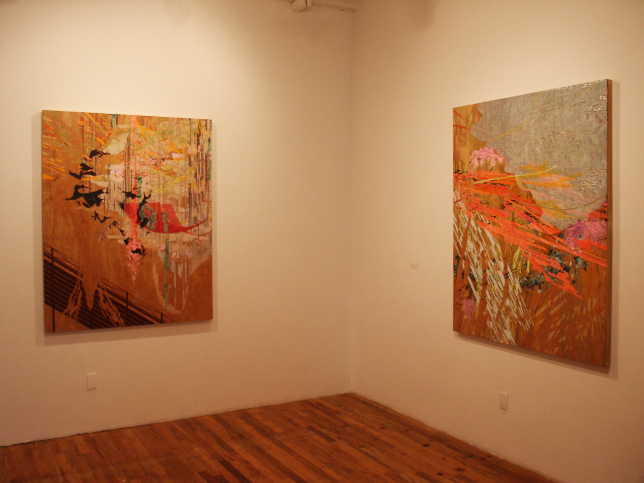 Two paintings hung on white walls meeting in a corner. The paintings are colorful, predominantly pink and red.