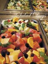 A fruit salad with watermelon, oranges, berries, and more in a metal dish, as if at a deli station. Overlaid white text in script reads 