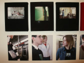 Photographs hung on a wall in two rows. The top row photographs are outlined in black and show images of people inside an apartment. The bottom row photographs show people on a subway.