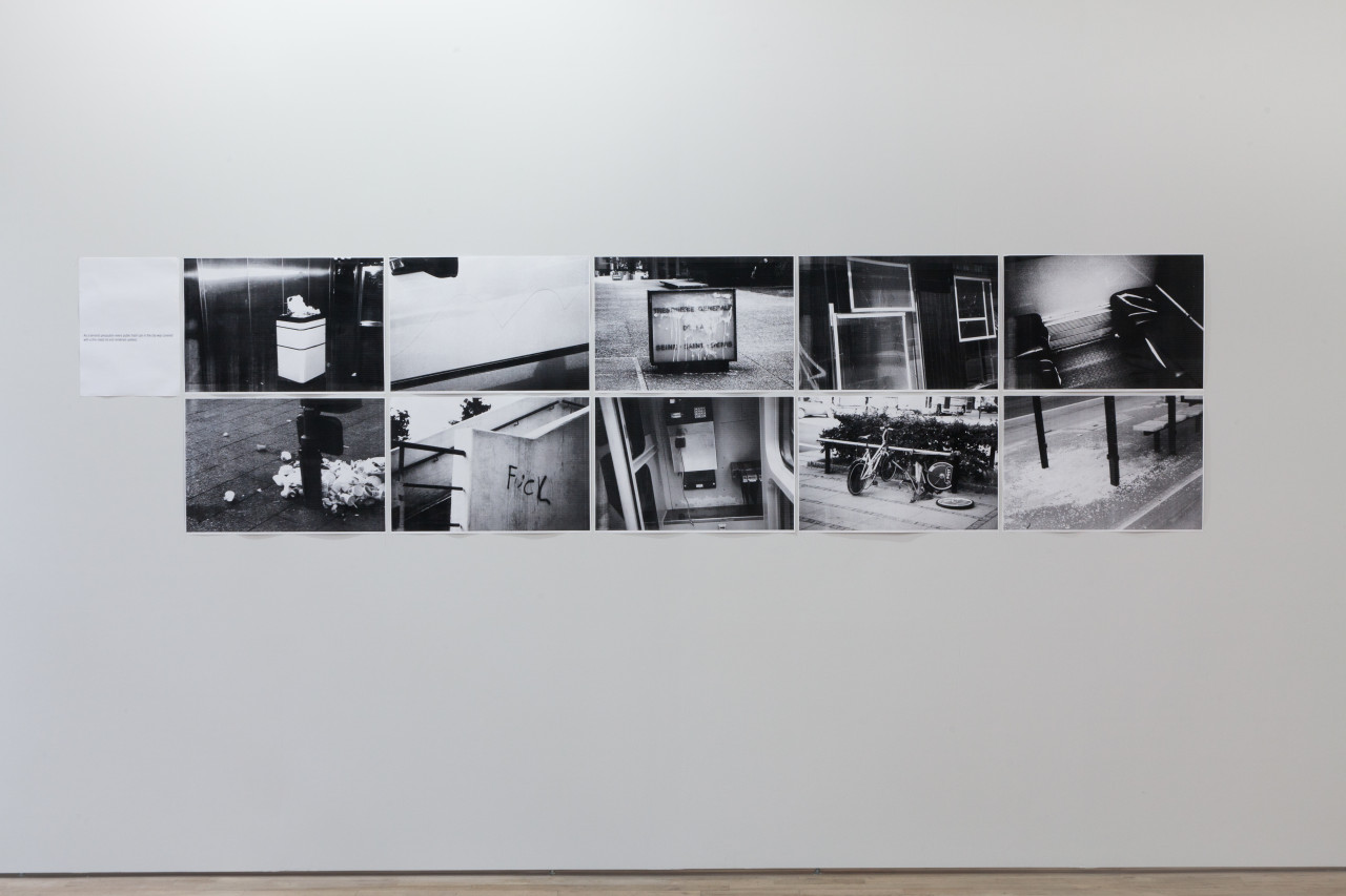 Ten black and white photographs arranged in a rectangle on a white wall. The images show various scenes of assorted trash on streets.