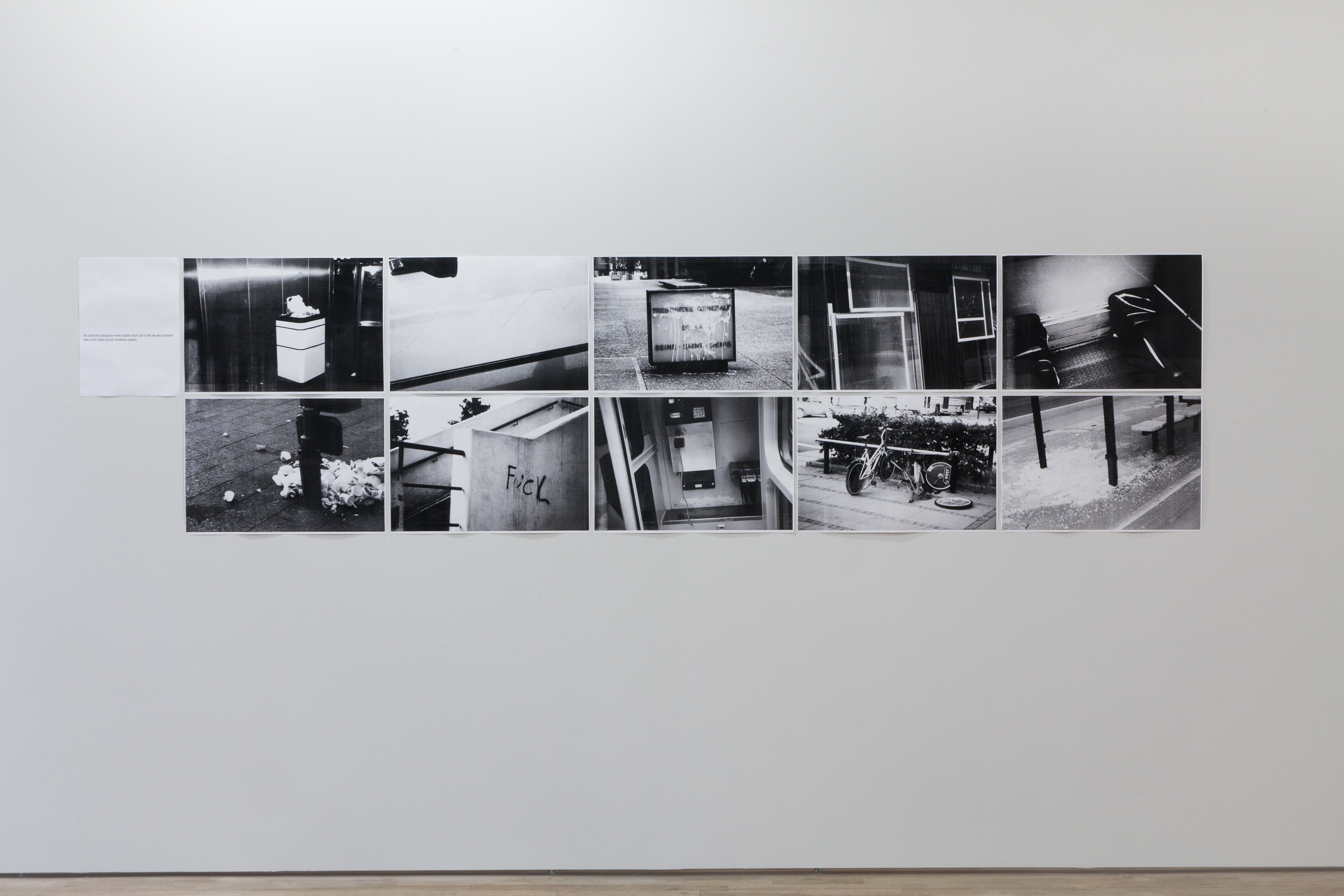 Ten black and white photographs arranged in a rectangle on a white wall. The images show various scenes of assorted trash on streets.