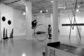 A photograph of a large gallery.  In the center of the room, a person gazes at large, geometric sculptures.