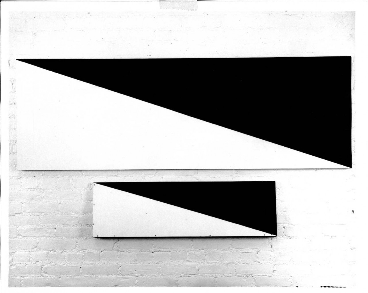 A photograph of one large painting divided evenly diagonally across in black and white above a smller painting that does the same.
