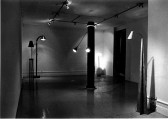 A black-and-white photograph of a gallery space with several floor lamps installed throughout.