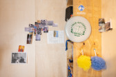 Various photographs of athletes and other personal images are arranged on a light wooden wall to the left. A wooden shelf sits against the right wall, shown in profile. A frisbee and two loofahs hang off the side of the shelf, with other stickers and printed images arranged on the walls.