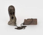 On the left is an oblong ceramic sculpture of a ghost with its mouth open. In the ghost's left hand is a coiled chain. The other end of the chain is wrapped around a worn down brick that reads 