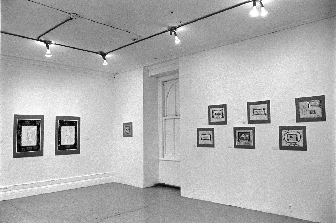 View of drawings mounted to white walls. Small labels accompany each drawing, taped to the walls.