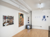 A diagonal view of photographs, paintings, sculptures, and prints against two walls. In the corner rests a TV displaying a person with their back turned.