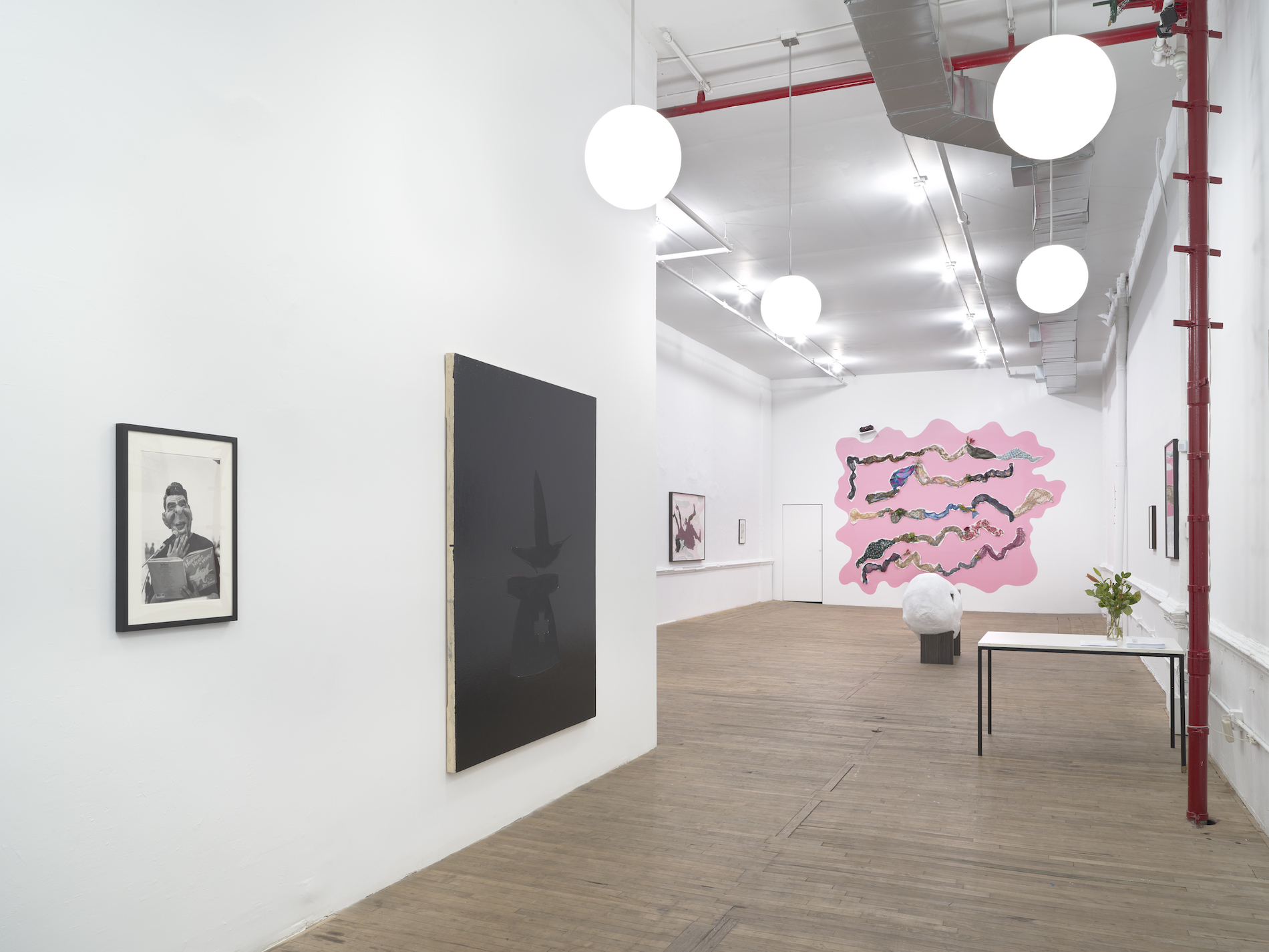An angled view of paintings and photographs against multiple walls. In the background, a pink wall installation is mounted.