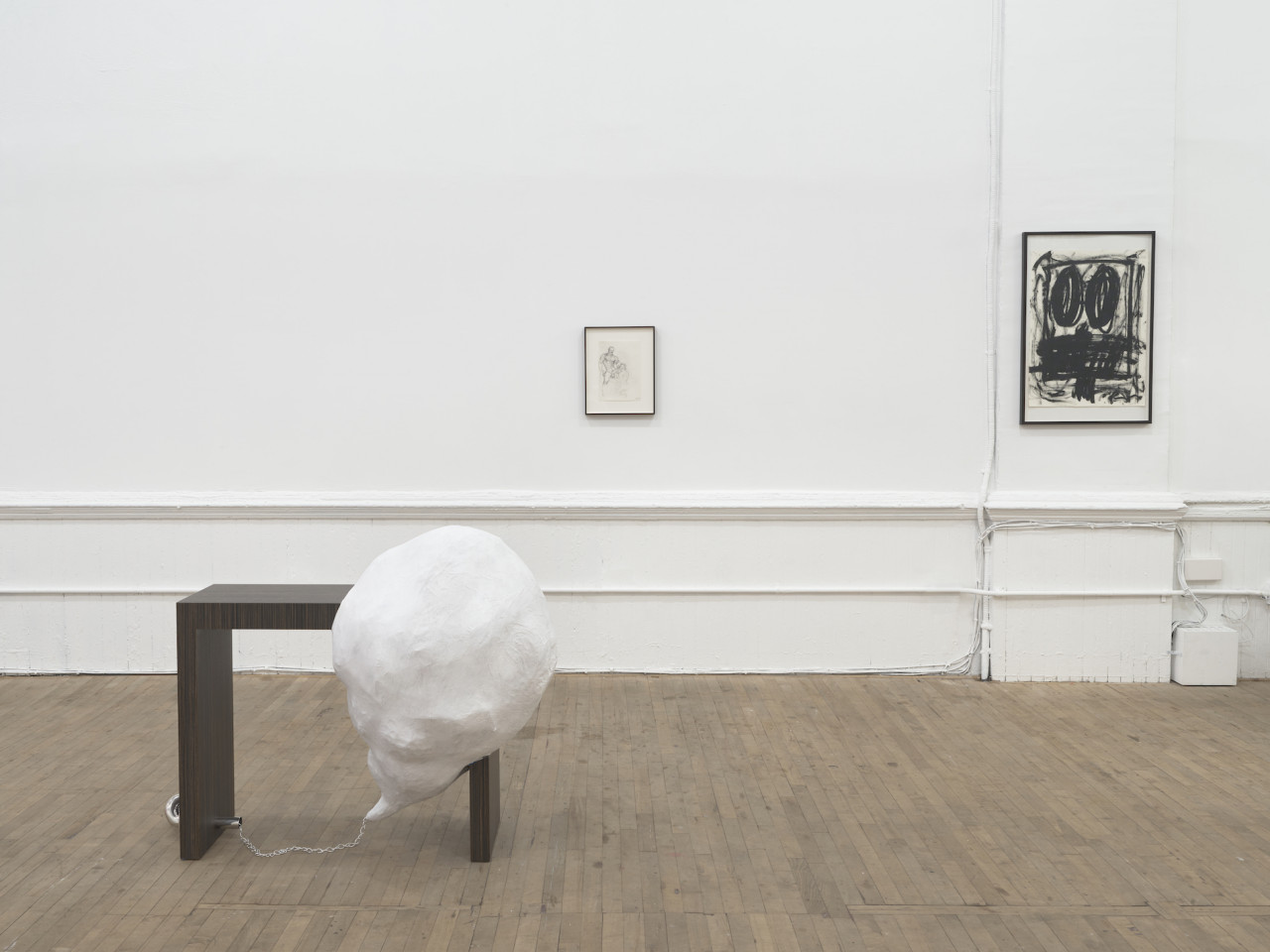 A wooden bench with a white, dome-like structure attached to its corner. Two framed drawings hang on the wall in the background.