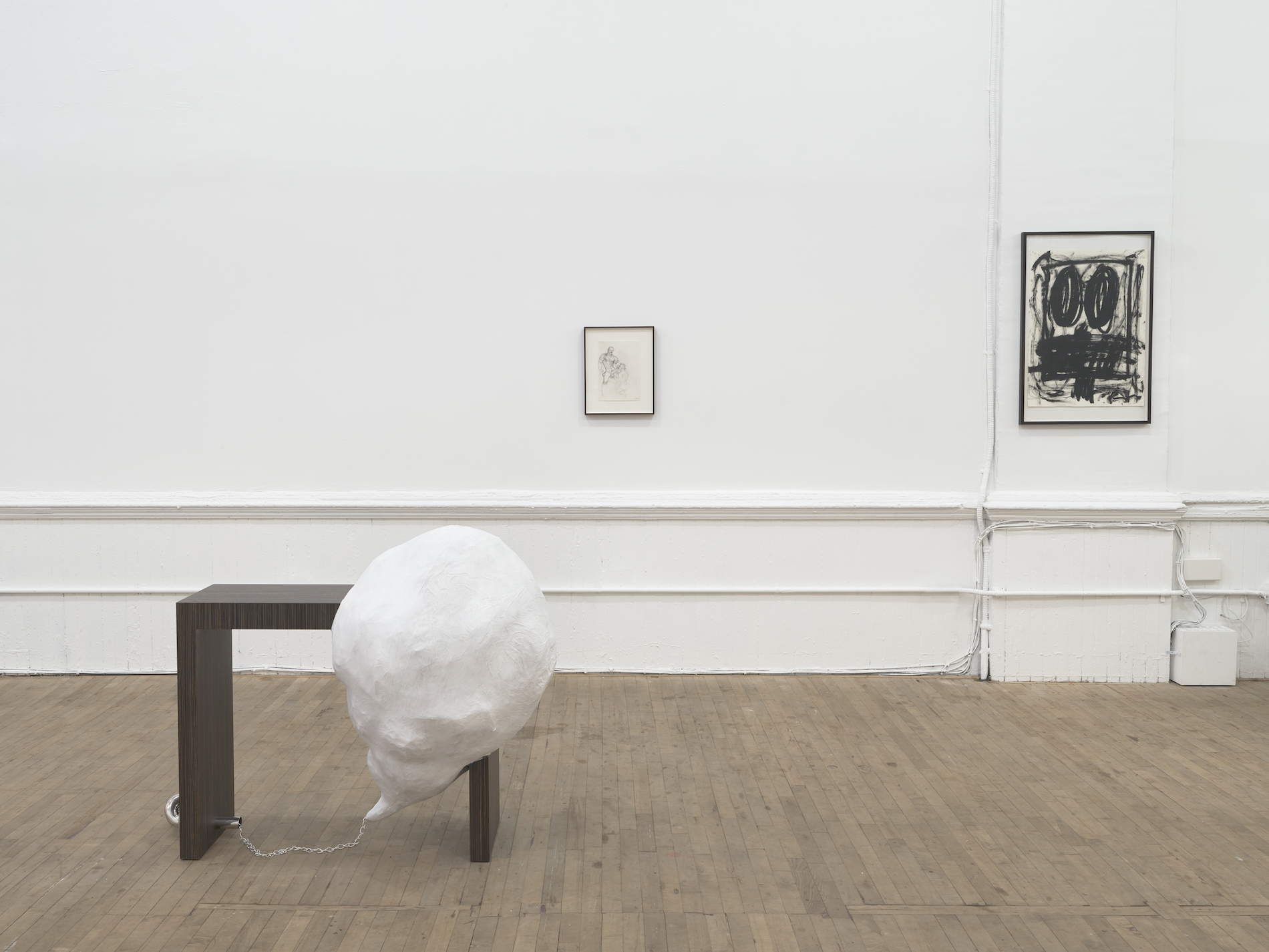 A wooden bench with a white, dome-like structure attached to its corner. Two framed drawings hang on the wall in the background.