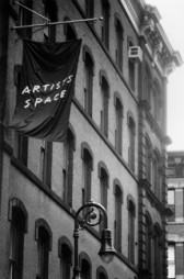 A black and white image of a building. A black flag hangs that reads, 