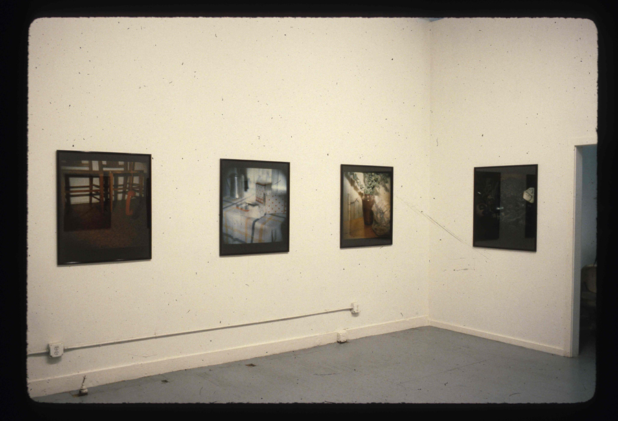Photographs of different housing interiors hang in a white-walled gallery space.