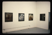 Photographs of different housing interiors hang in a white-walled gallery space.